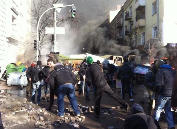 Protesters throw stones at police as firefighters try to put out a fire to a building on 17/5 Institutska St., where officers had been firing from the rooftop down on a crowd of demonstrators.