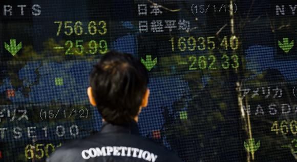 A man looks at an electronic board displaying Japan's Nikkei average (top R) in Tokyo January 13, 2015.