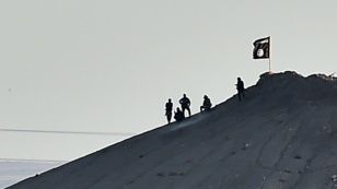 Сириядағы Кобани қаласы маңында «Ислам мемлекеті» тобының жалауы қасында тұрған адамдар. 7 қазан 2014 жыл. (Көрнекі сурет)